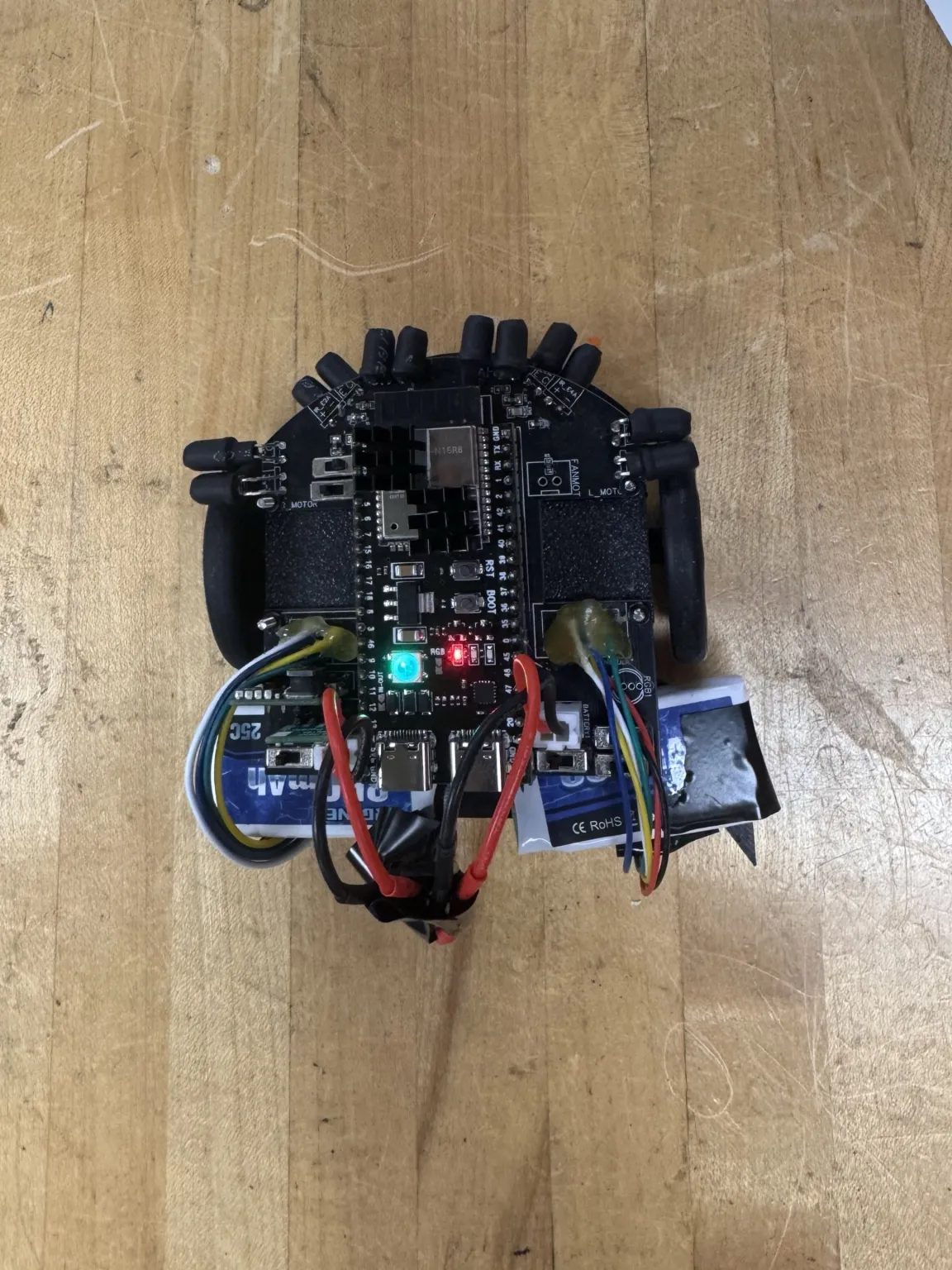 Antigravitieee from above: a black PCB with an ESP32-S3 board in the middle, six IR sensors in black heat-shrink around the front and a LiPo battery at the back